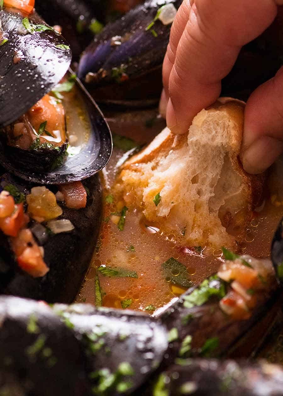 Crusty bread being dipped into mussel sauce