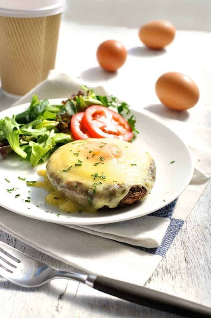 Baked Eggs in Mushrooms covered in melted cheese on a white plate with coffee on the side, ready to be eaten.