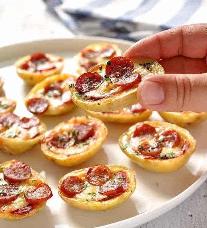 Close up of a hand holding a Mini Pizza Potato Skin with a platter of Mini Pizza Potato Skins in the background.