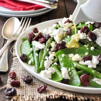 Dressing being poured over a Christmas Salad made with snow peas, asparagus, beans, feta and cranberries. Colours of Christmas!