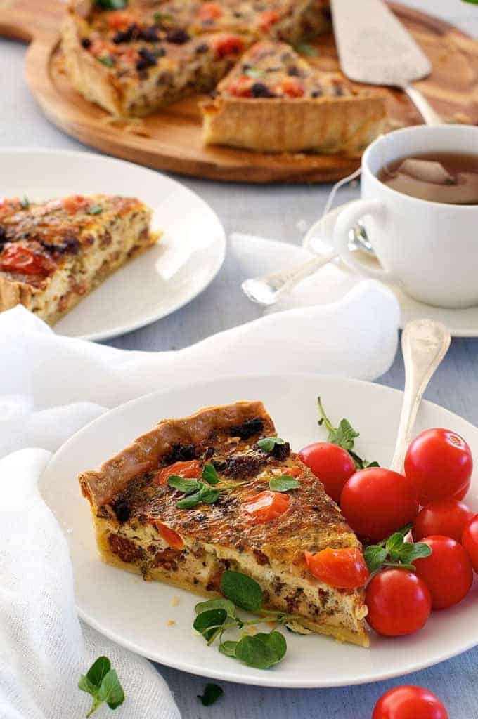 A slice of Italian Sausage Quiche with cherry tomatoes on the side