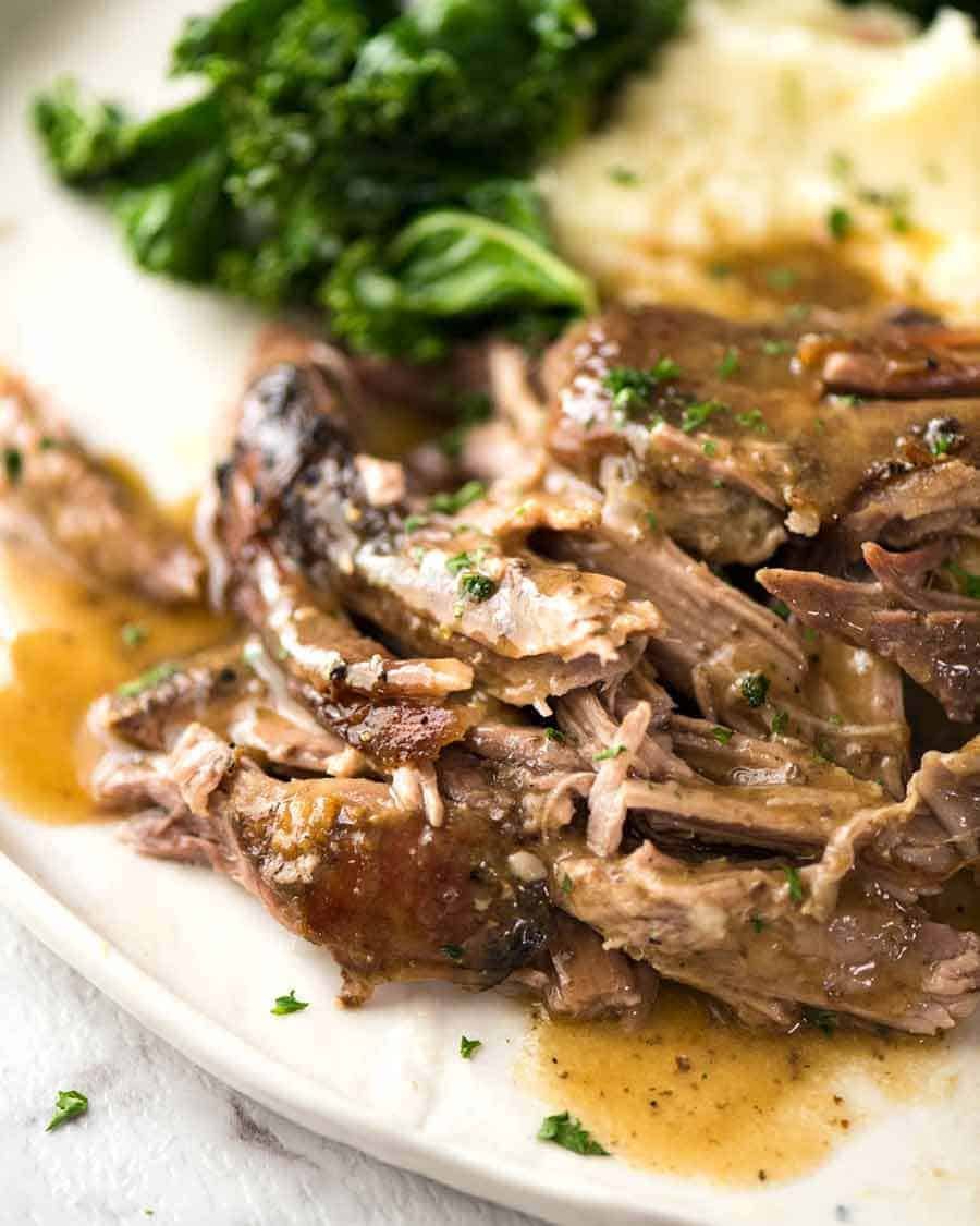 Tender Slow Roast Leg of Lamb with gravy on a plate with a side of potato and steamed greens