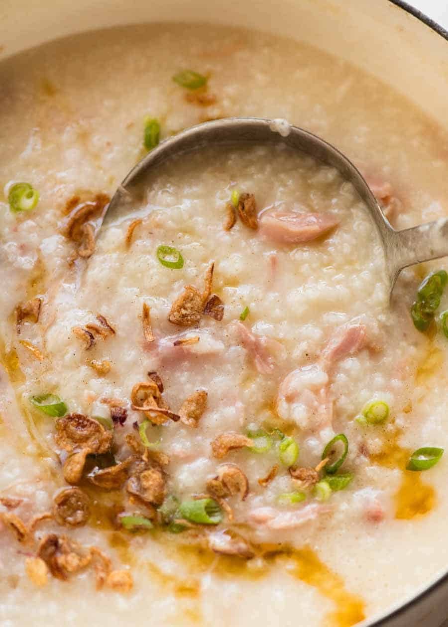 Chinese Ham Bone Rice Soup (Congee) being ladled out of a white pot, fresh off the stove