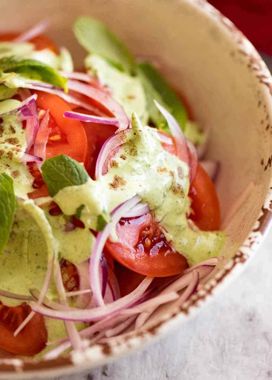 Close up of Indian Tomato Salad drizzled with Mint Dressing in a rustic cream bowl, ready to be served