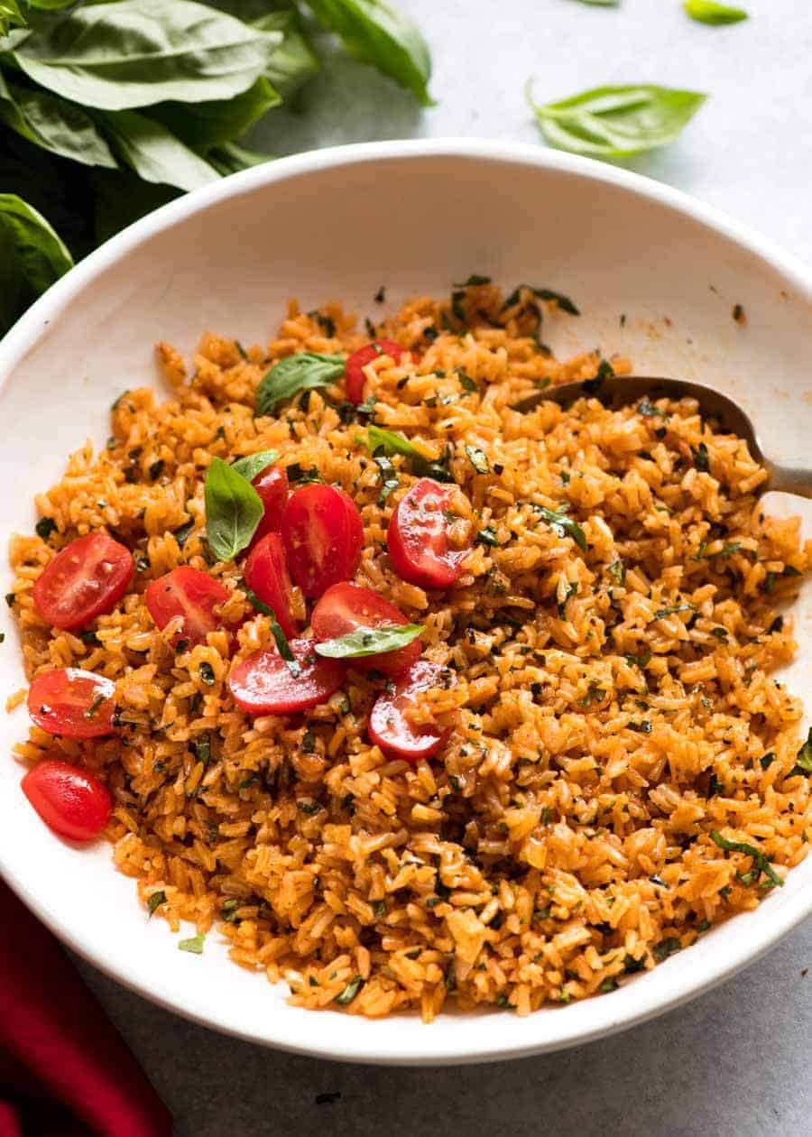 Pile of Tomato Basil Rice in a white bowl garnished with fresh tomato and basil, ready to be served