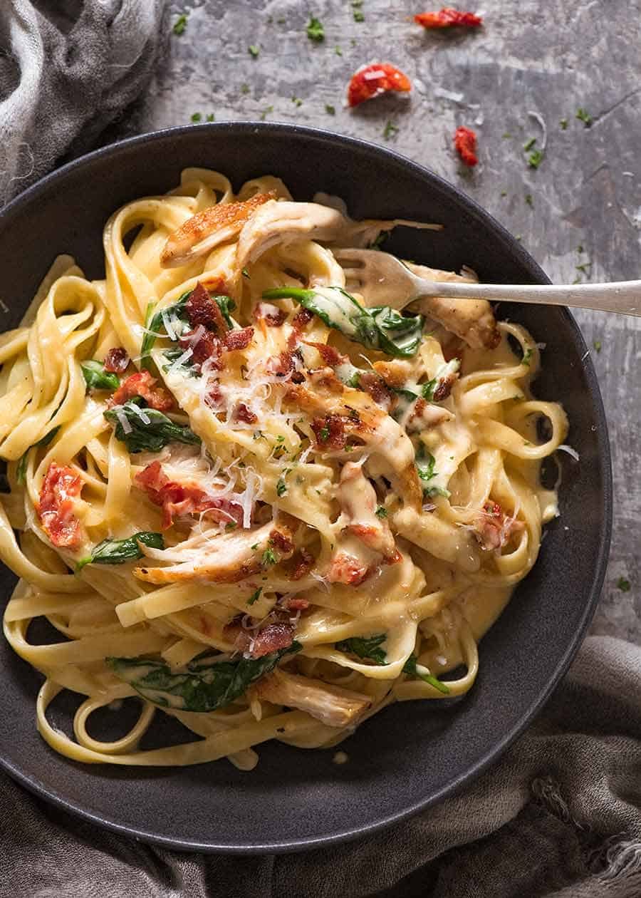 Overhead photo of Chicken Pasta recipe with creamy alfredo sauce, sun dried tomato, spinach and bacon in a rustic black bowl, ready to be eaten