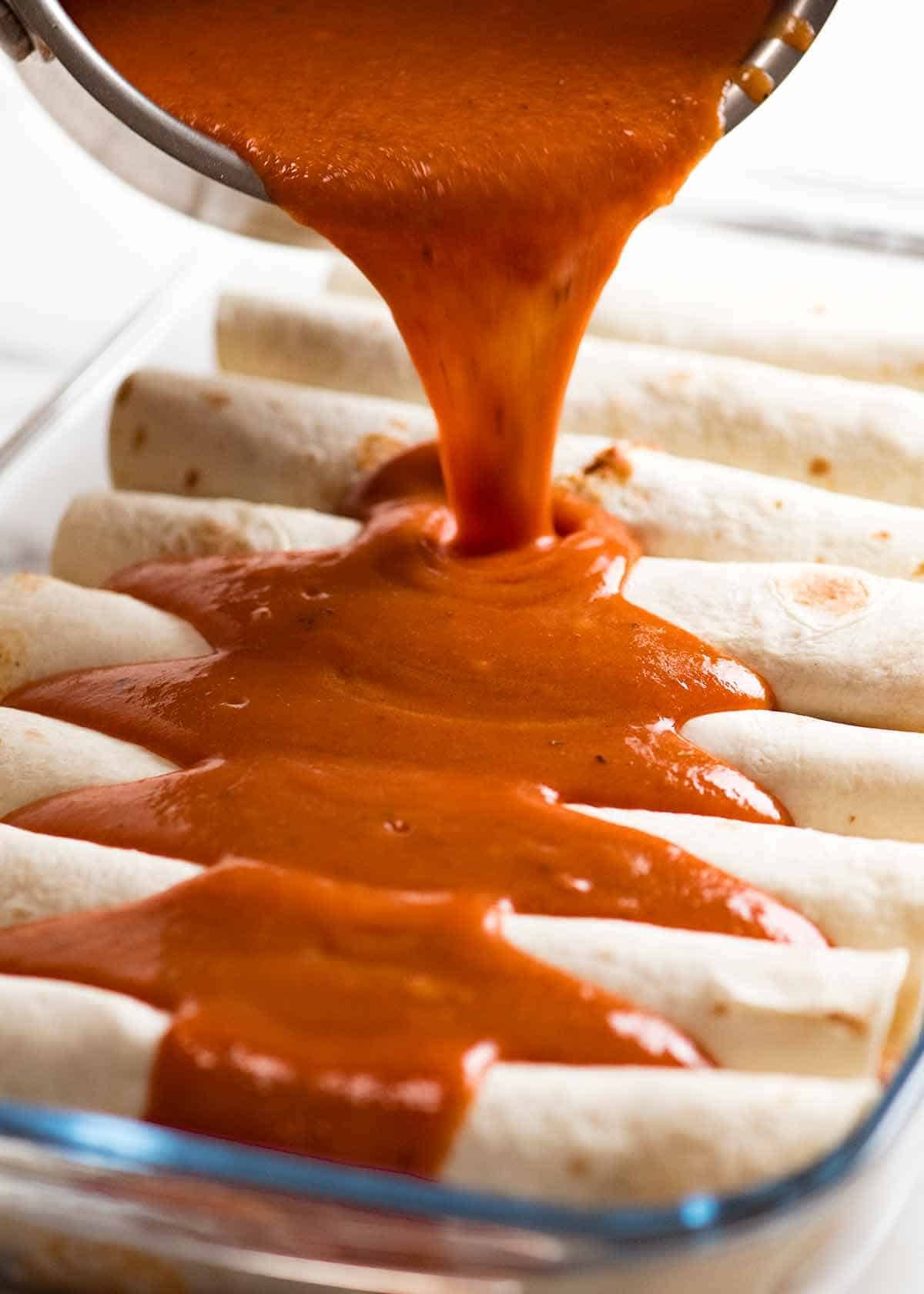 Pouring enchilada sauce over Chicken Enchiladas