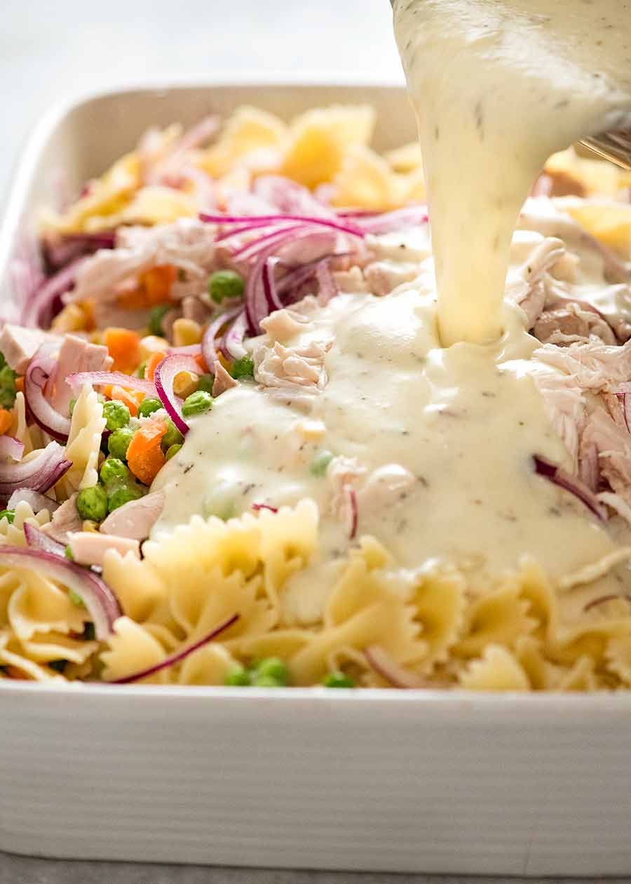 Pouring creamy sauce over pasta, chicken and vegetables