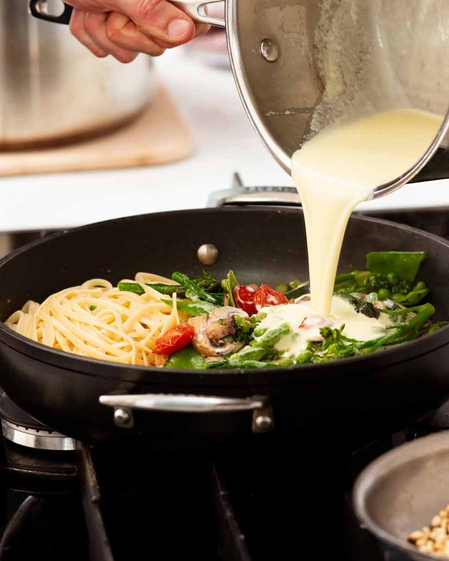 Pouring cream sauce over Pasta Primavera
